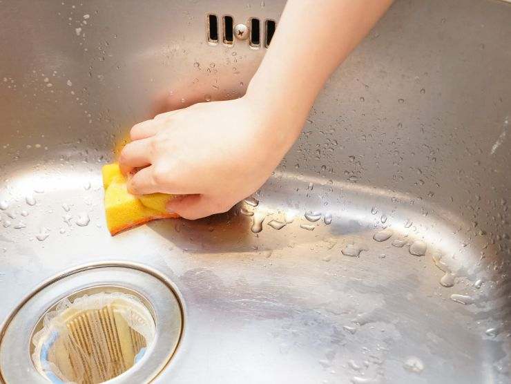 persona che pulisce lavandino in acciaio della cucina