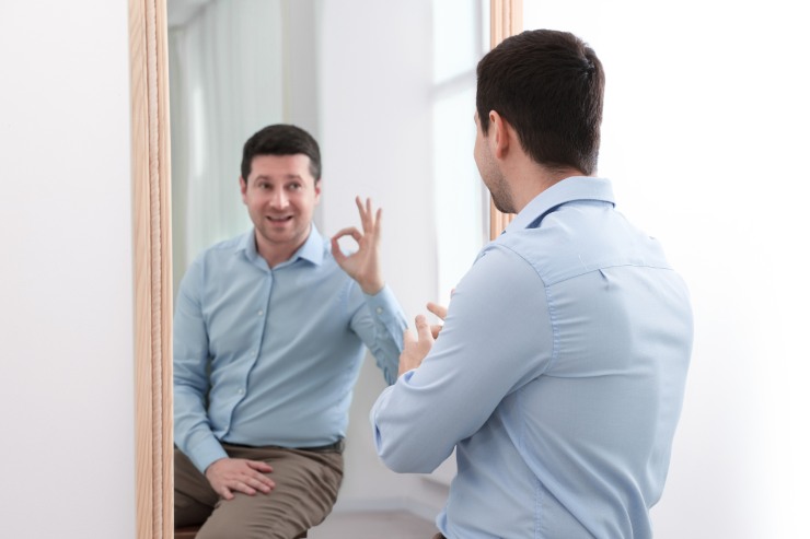 Un omo che si specchia ed il suo riflesso fa un cenno di "ok"