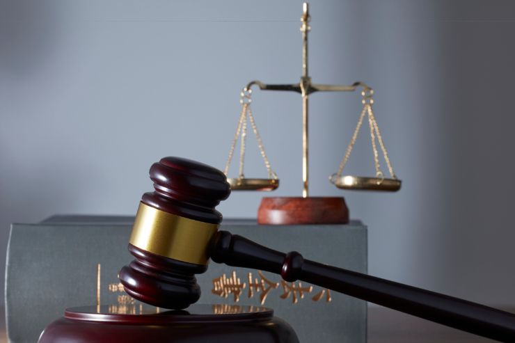 Una bilancia sopra un libro di legge ed un martello da giudice in primo piano