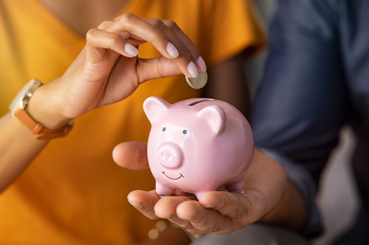 Una ragazza che mette una moneta nel salvadanaio che tiene un ragazzo in mano