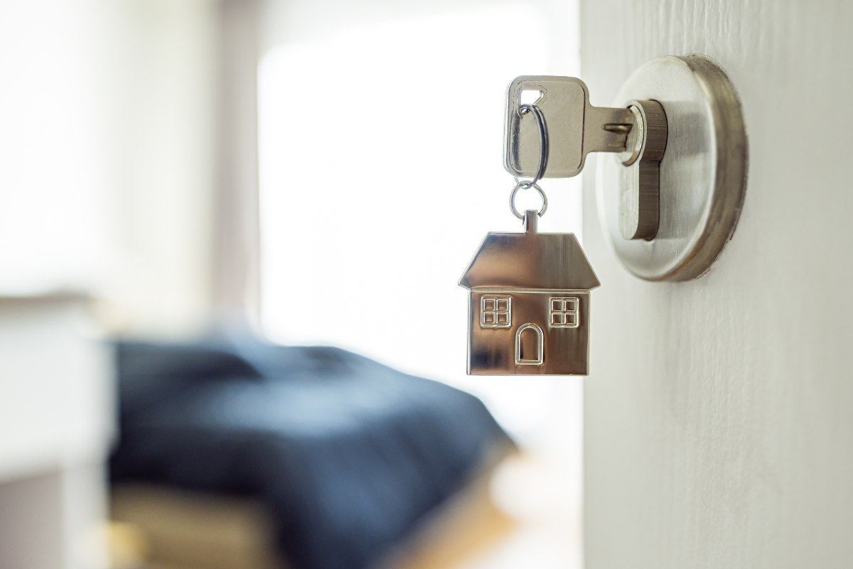 Una porta di casa mezza aperta con inserite nella serratura delle chiavi con un portachiavi a forma di casa