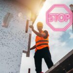 Un operaio che sta installando un cappotto termico ed un segnale di stop in alto a destra