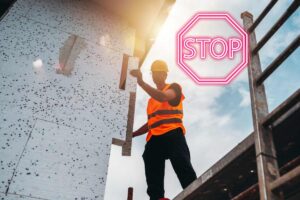 Un operaio che sta installando un cappotto termico ed un segnale di stop in alto a destra