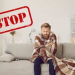 Una persona sul divano con una coperta che sente freddo ed una scritta in alto a sinistra che dice "Stop"