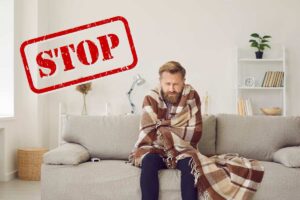 Una persona sul divano con una coperta che sente freddo ed una scritta in alto a sinistra che dice "Stop"