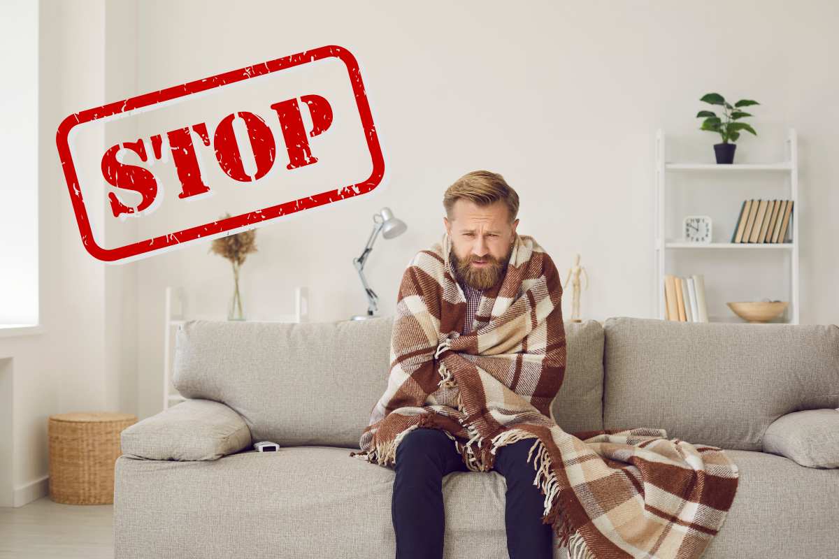 Una persona sul divano con una coperta che sente freddo ed una scritta in alto a sinistra che dice "Stop"