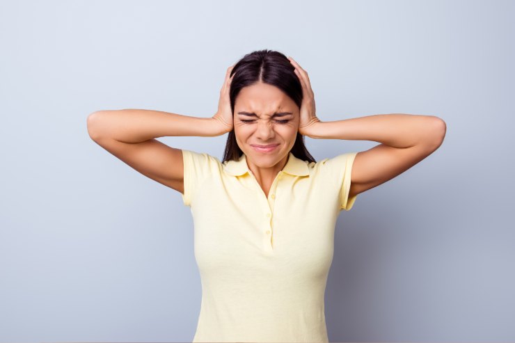 Una donna che si tappa le orecchie con le mani per via del troppo rumore