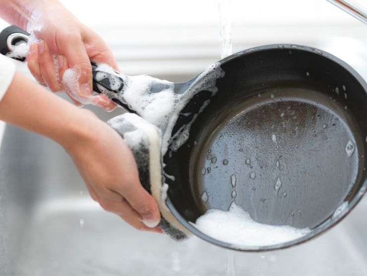 mani che lavano una padella nera