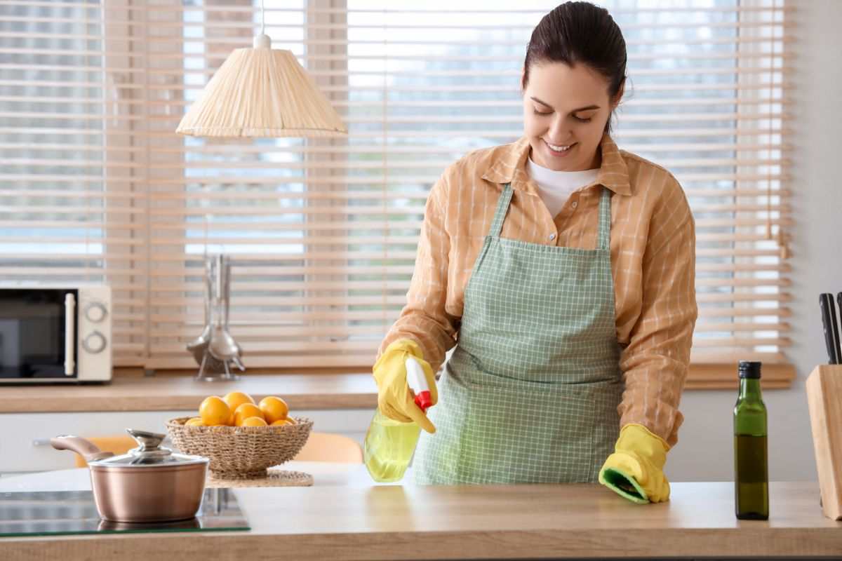 donna che spruzza uno spray per pulire il piano della cucina