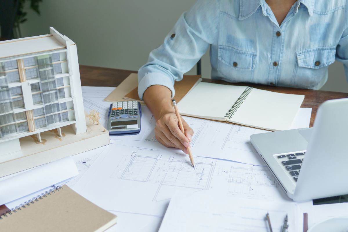 Un architetto che progetta una casa con fogli di carta, un computer e miniature di casa