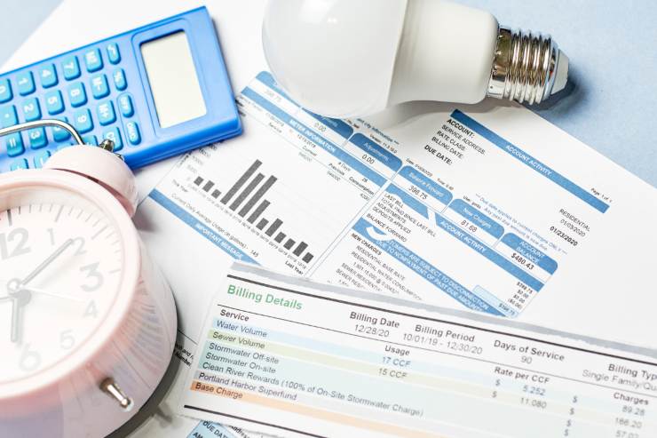 Un tavolo con sopra documenti, bollette, calcolatrice, sveglia e una lampadina