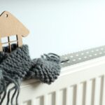 Un modellino di una casa in legno avvolto da una sciarpa e sopra un termosifone