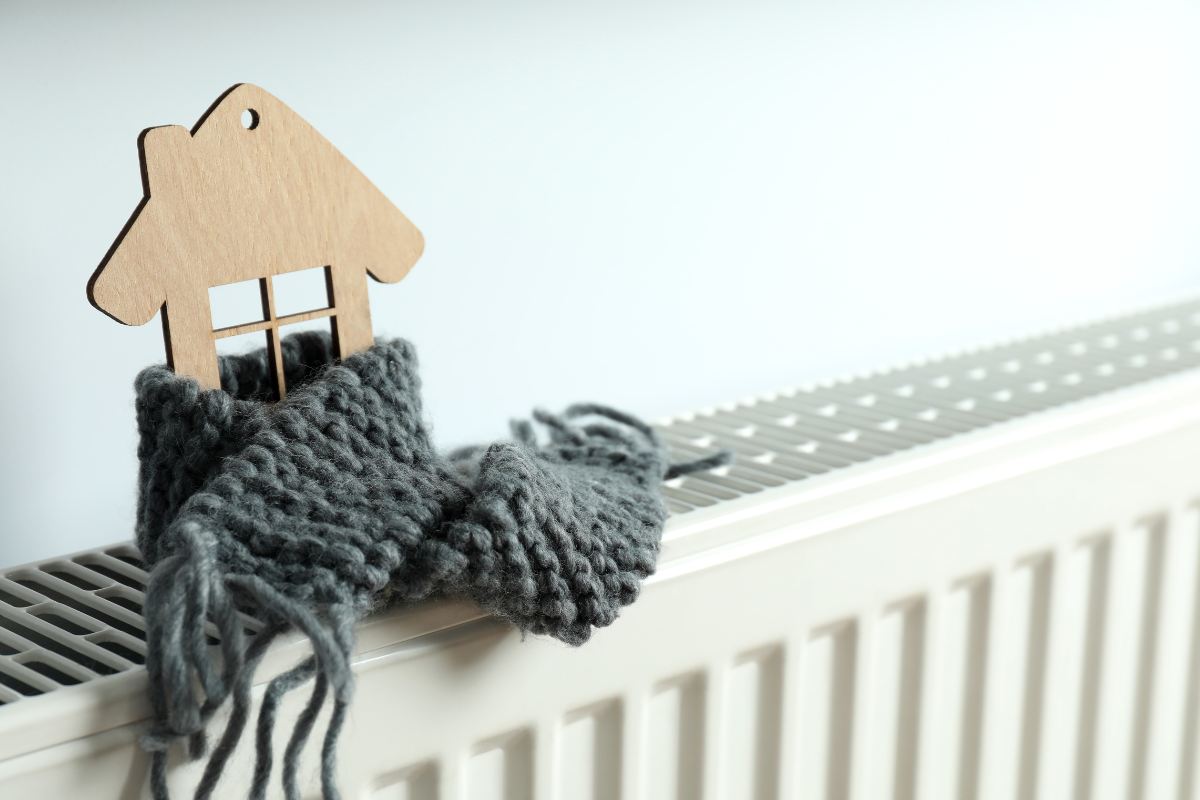 Un modellino di una casa in legno avvolto da una sciarpa e sopra un termosifone