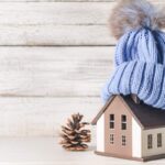 Una miniatura di una casa con sopra un cappuccio di lana ed una pigna accanto