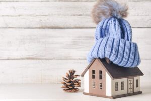 Una miniatura di una casa con sopra un cappuccio di lana ed una pigna accanto