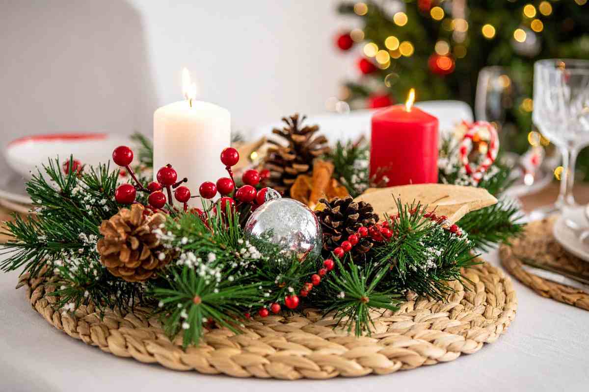 una tavola con il centrotavola natalizio fai da te con pigne, candele e palline di Natale