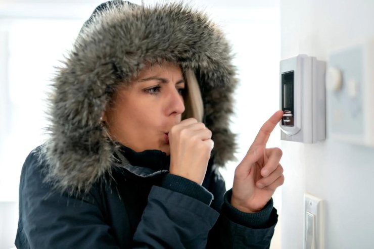 Una donna con il giubbotto che sente freddo che imposta il termostato della casa