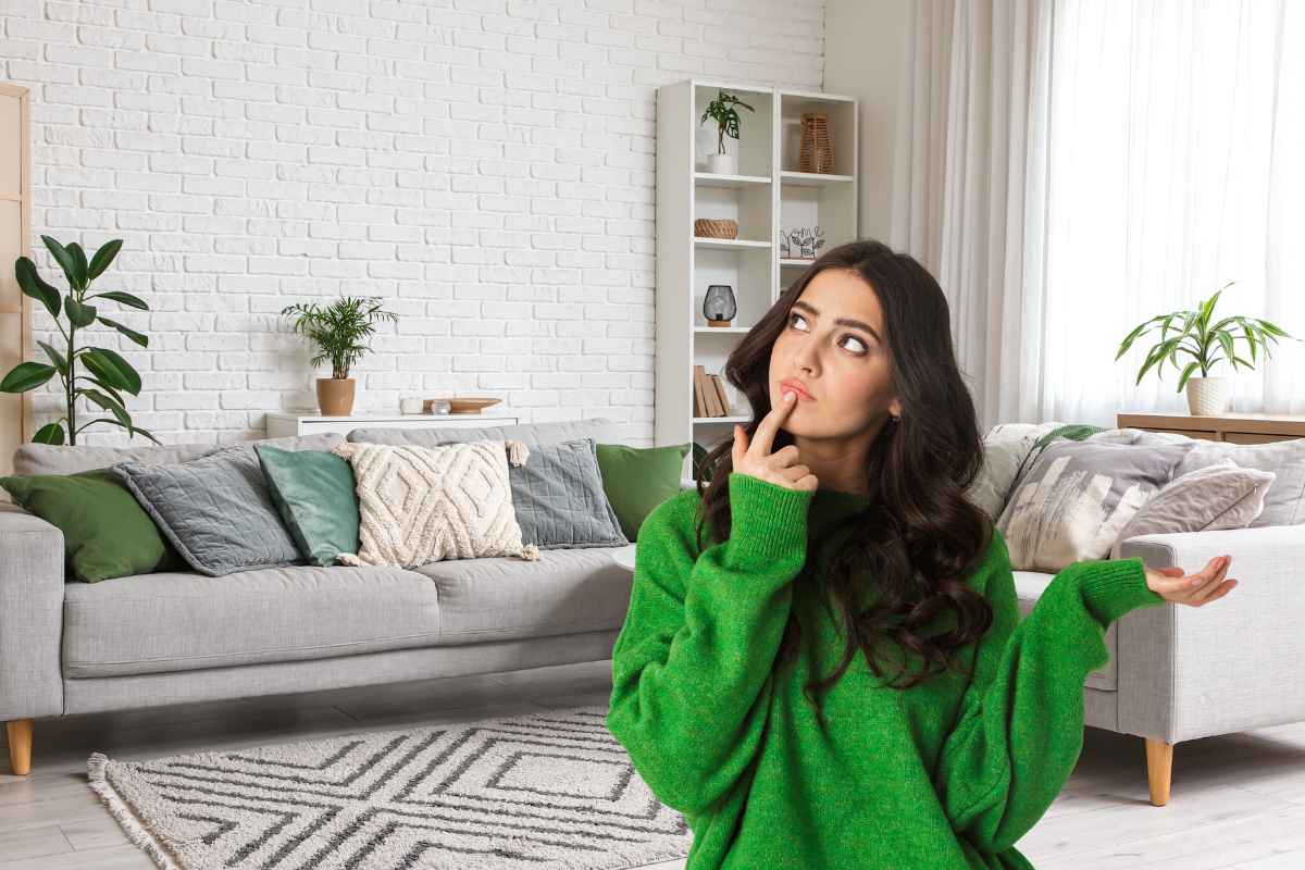 Un salone con un divano con sopra cuscini e una ragazza in primo piano che è dubbiosa