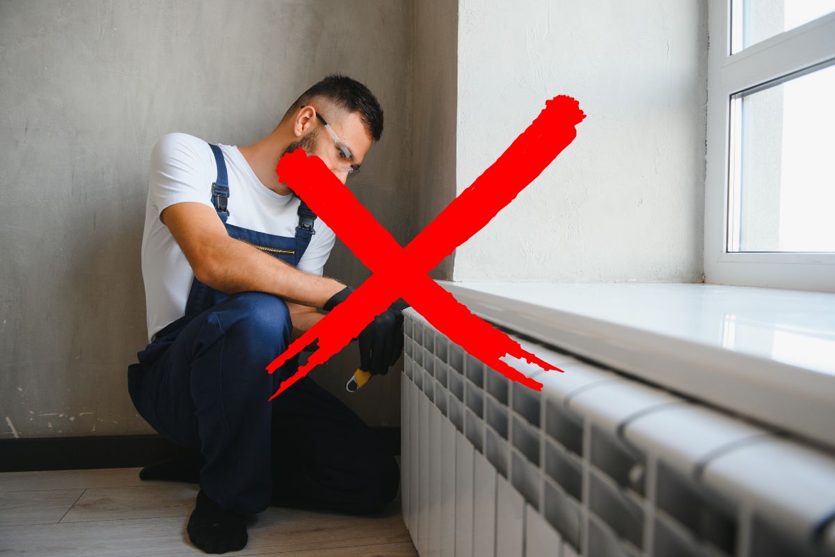 Un operaio che sta smontando un termosifone con una X rossa in primo piano