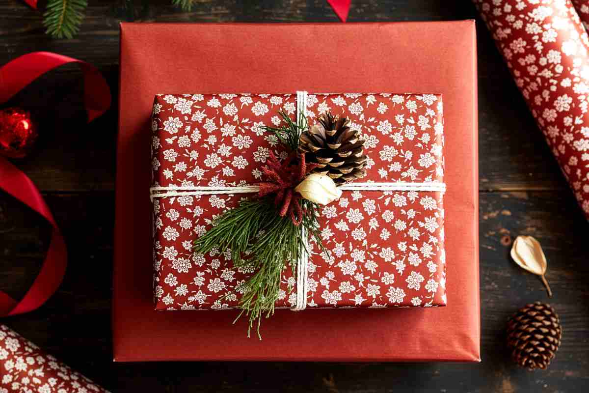 un pacchetto regalo con carta natalizia rossa e una pigna portafortuna