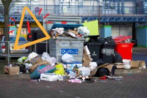 Un cassonetto dell'immondizia pieno di rifiuti differenti e sparsi ovunque