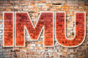 Questa immagine presenta l'acronimo IMU (Imposta Municipale Unica) in grandi lettere bianche con un effetto di riempimento color rosso-arancio, sovrapposto a un muro di mattoni rossi. L'acronimo si riferisce all'imposta patrimoniale italiana sugli immobili.