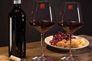 una tavola con due calici da vino, bottiglia e piatto con uva e noci