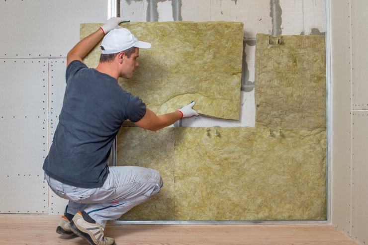 Un uomo che sta mettendo sul muro dei pannelli isolanti 