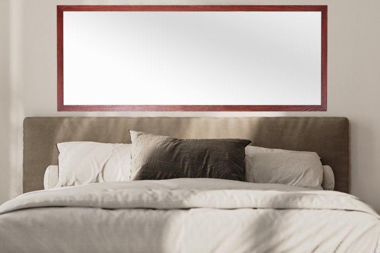 Un letto ed il muro su cui poggia il letto decorato con uno specchio orizzontale