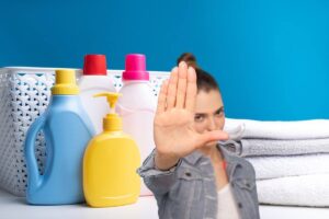 in primo piano una donna che dice stop con la mano e sullo sfondo si possono vedere dei prodotti per la pulizia del bucato e degli asciugamani piegati