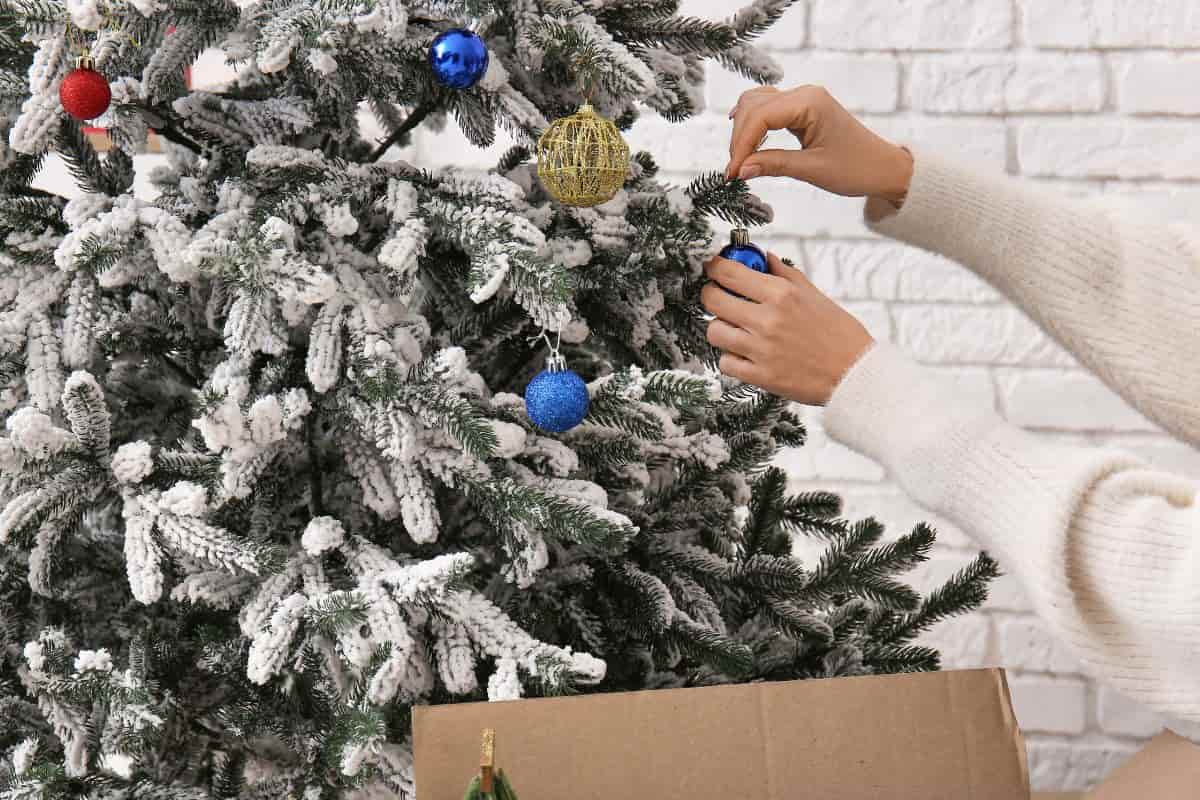 Mani che decorano albero di Natale innevato