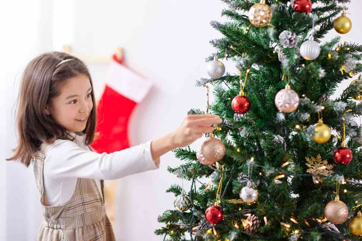 Bambina che appende pallina all'albero di Natale