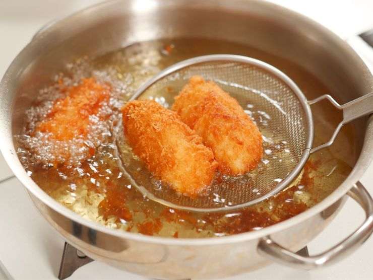 pentola di acciaio piena d'olio in cui stanno friggendo dei crocché di patate