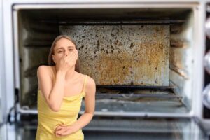fornetto pieno di sporco e d'incrostazioni e donna in primo piano che si tappa naso e bocca per il disgusto