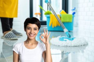 sfondo di una donna che usa il mocio per pulire il pavimento e in primo piano c'è una donna che fa ok