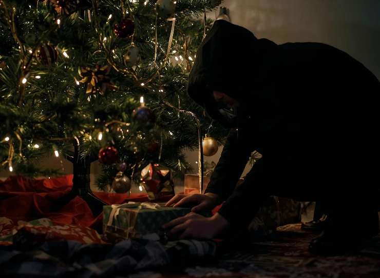 ladro che cerca qualcosa sotto l'albero di natale pieno di regali 