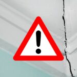 una crepa bella evidente nella parete e in primo piano un segnale di pericolo