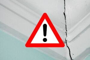 una crepa bella evidente nella parete e in primo piano un segnale di pericolo