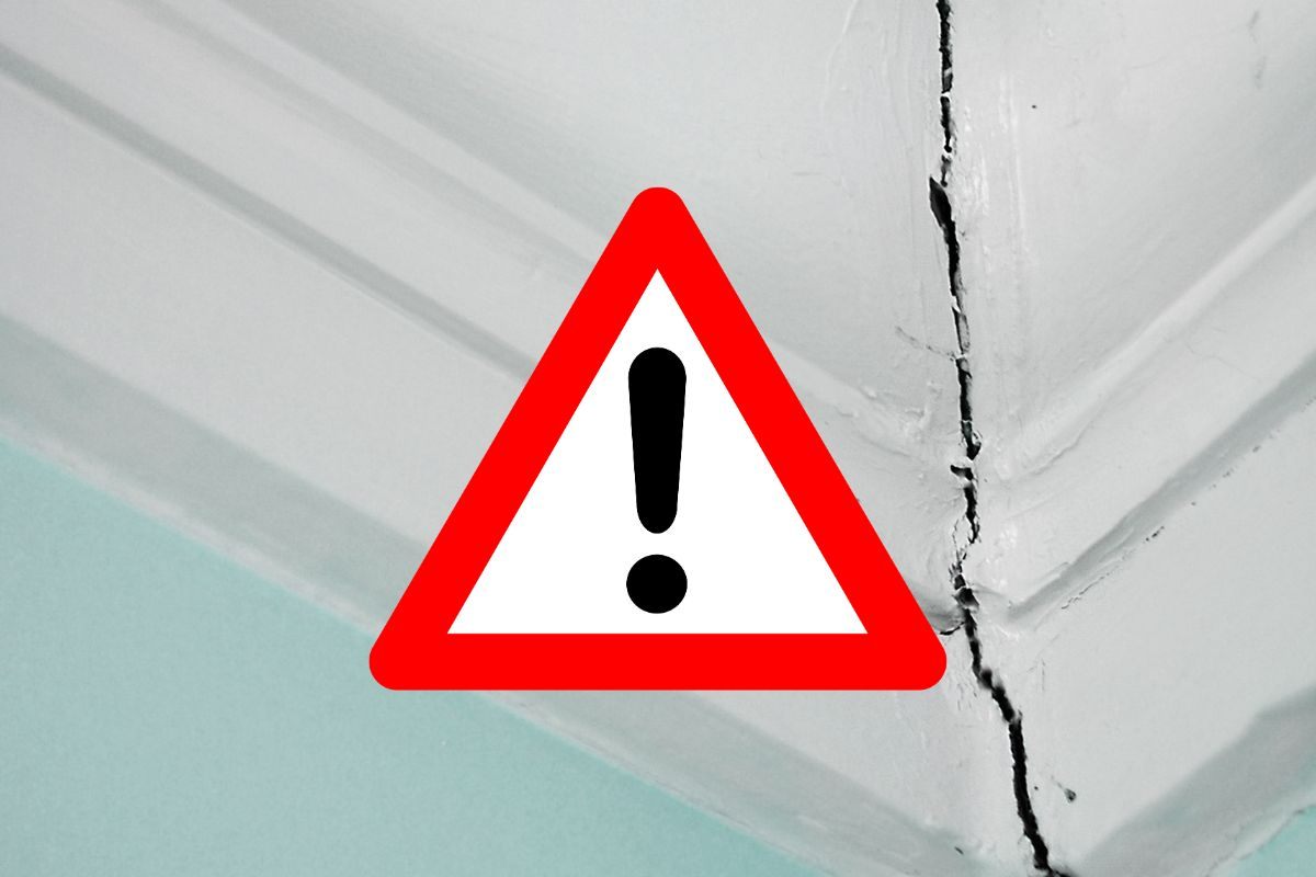 una crepa bella evidente nella parete e in primo piano un segnale di pericolo