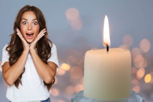 donna con volto stupito e mani sul volto vicino a candela bianca accesa