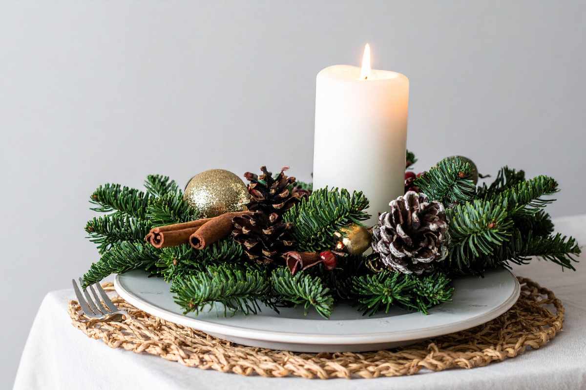 centrotavola con rami verdi, pigne e candela bianca accesa al centro 