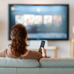 Una persona sul divano con il telecomando in mano che guarda la TV
