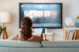Una persona sul divano con il telecomando in mano che guarda la TV