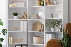 Primo piano di una libreria bianca con libri, elementi in rattan e piante