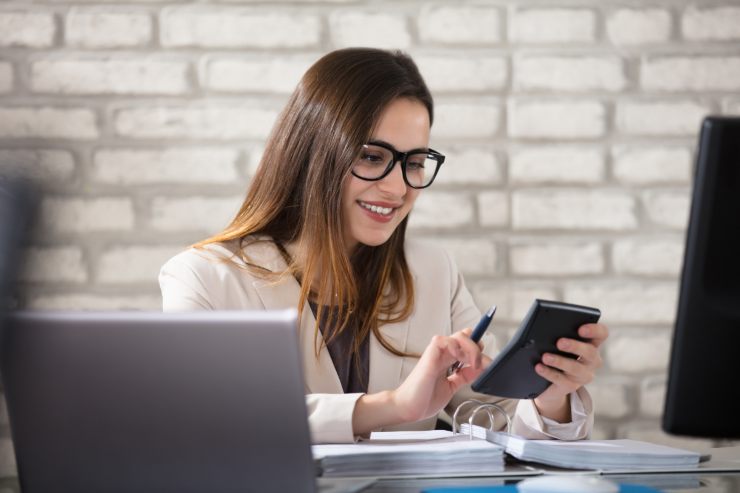 Una donna che fa i conti guardando documenti e usa una calcolatrice