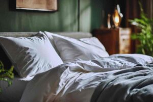 letto matrimoniale con federe chiare e copripiumino in una stanza dalle pareti verde salvia