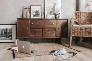 salotto con mobile in legno scuro con cassetti, poltrona in vimini e tappeto con compoter aperto per terra