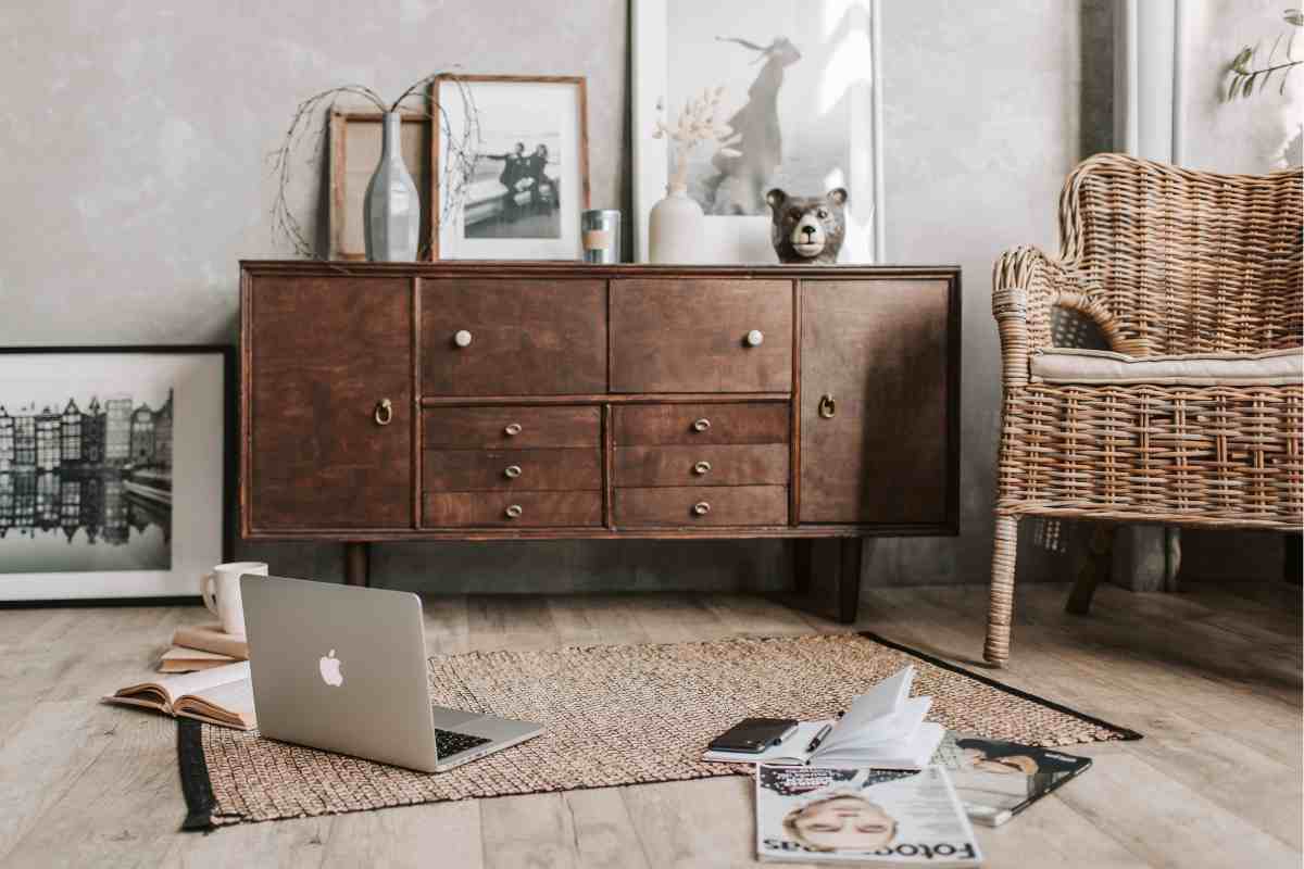 salotto con mobile in legno scuro con cassetti, poltrona in vimini e tappeto con compoter aperto per terra