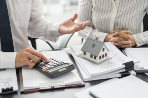 Delle persone che fanno ocnti e discutono di documenti con una miniatura di una casa