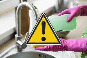 come sfondo una persona con guanti che mettere del detersivo per lavare i piatti e in primo piano un segnale di pericolo